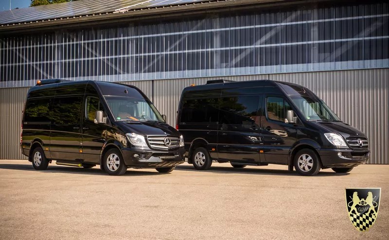 Two black Mercedes vans parked on a paved surface near a large building.