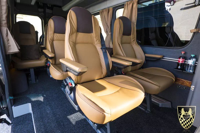Interior of a luxury van with tan leather seats and brown curtains.
