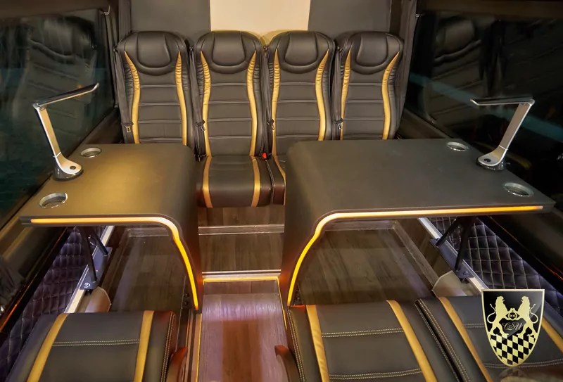 Luxury van interior with leather seats, two tables, cup holders, and ambient lighting.