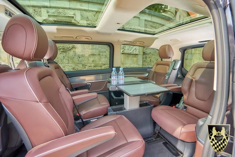 Spacious vehicle interior with brown leather seats and a foldable table, sunroof visible above.