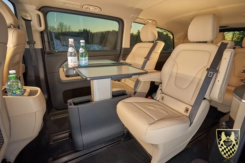 Luxurious van interior with beige leather seats, a central table, and bottled water.