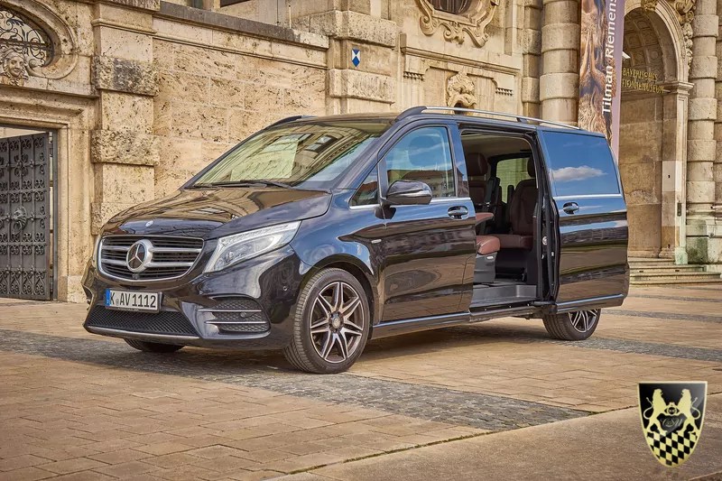 Black Mercedes van with sliding door open in front of an ornate building.