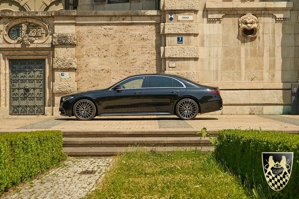 Black luxury sedan parked by stone building with ornate architecture.