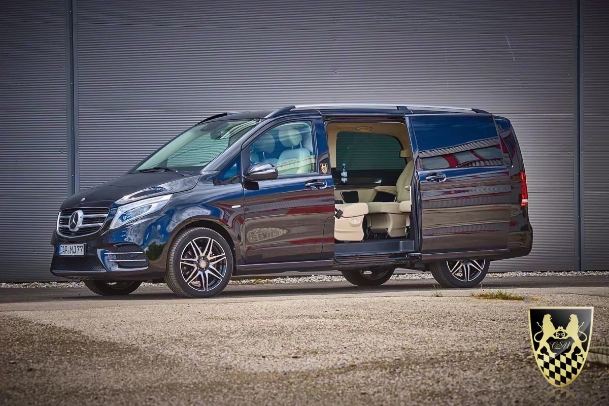 Black Mercedes van with open sliding door, parked on gravel.