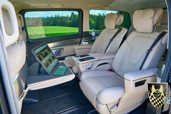 Luxurious van interior with beige leather seats and a fold-out table with a laptop.