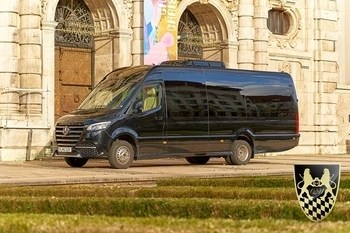 Black van parked in front of an ornate building with a coat of arms displayed.