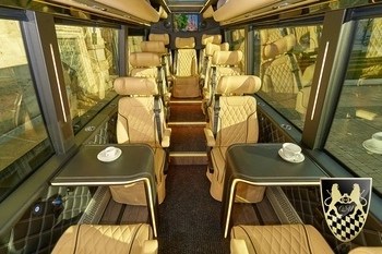 Luxury bus interior with beige seats, tables, and a crest on the door.
