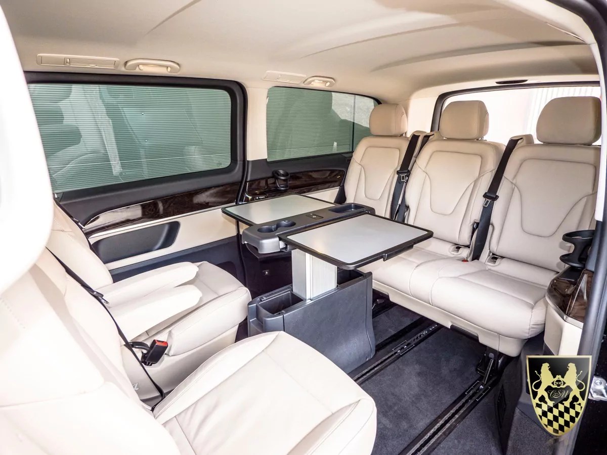 Luxury van interior with beige leather seats and fold-out tables.