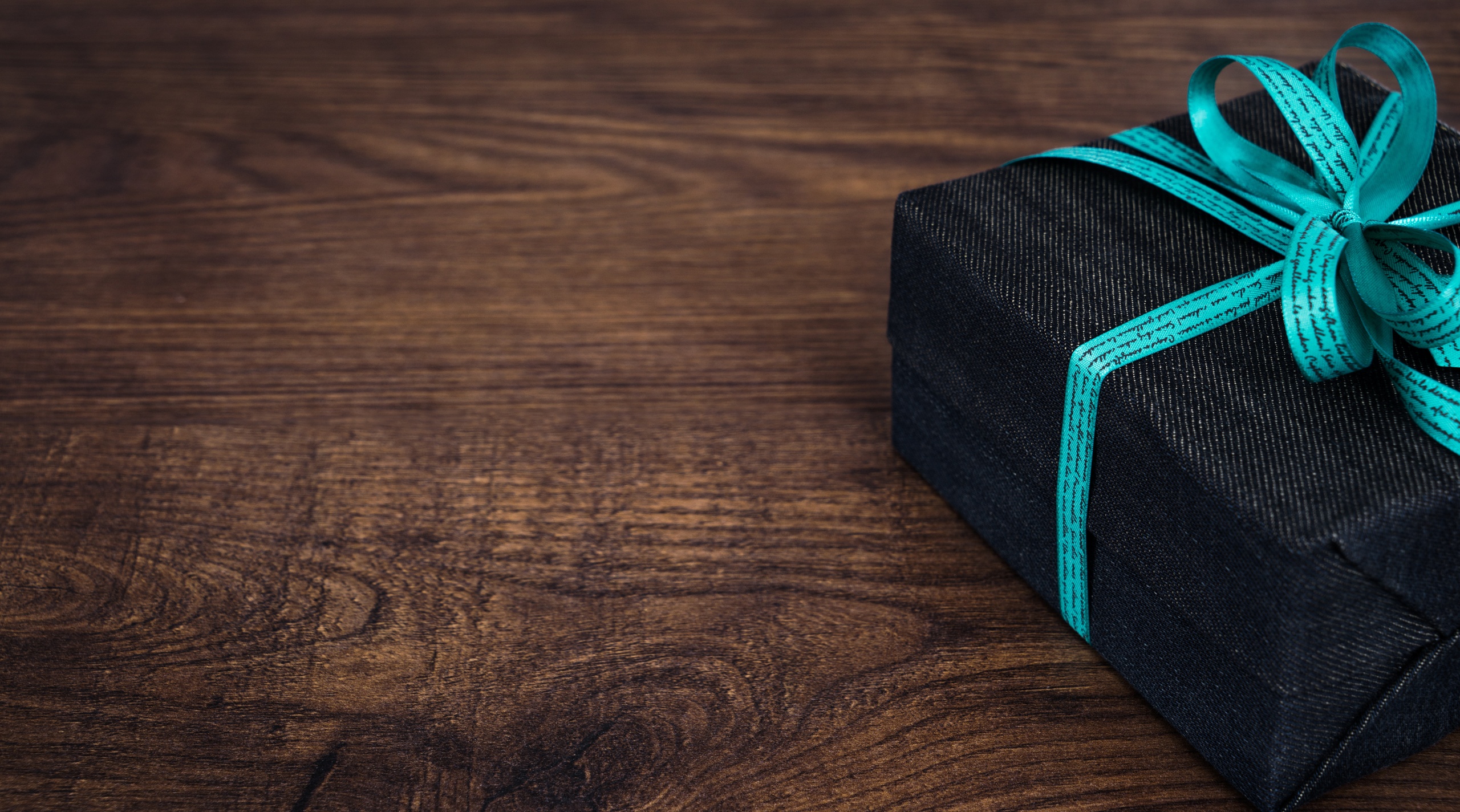 Black gift box with teal ribbon on wooden surface.
