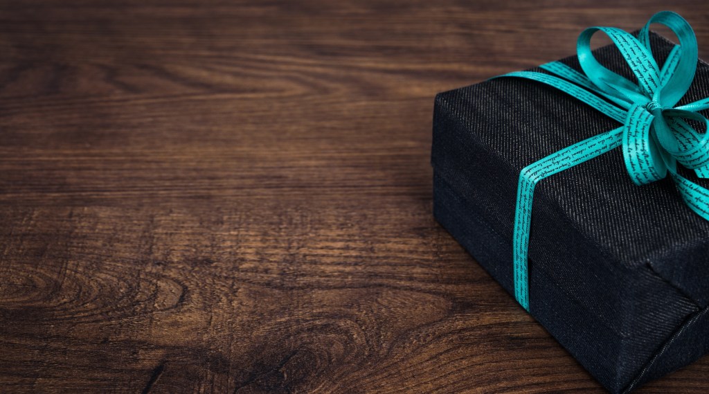 Black gift box with teal ribbon on wooden surface.