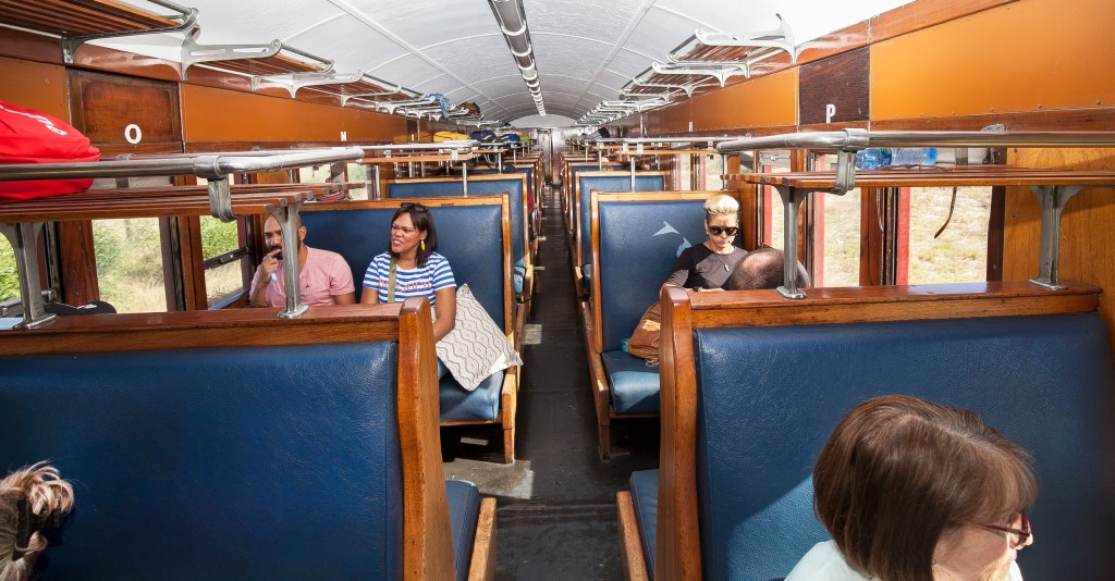 Interior of a vintage train with blue seats and passengers seated.