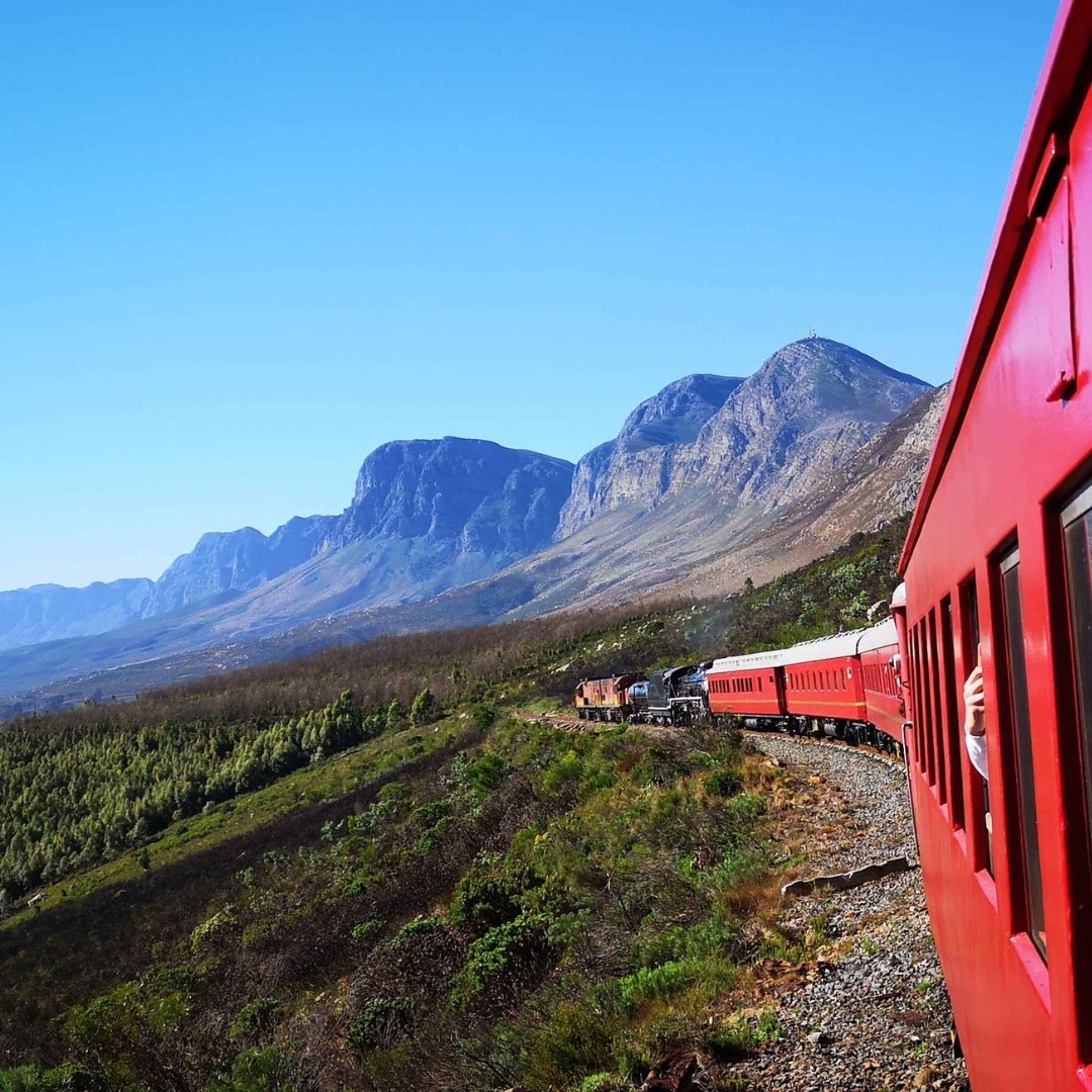 Red train traveling through mountains with scenic valley view.