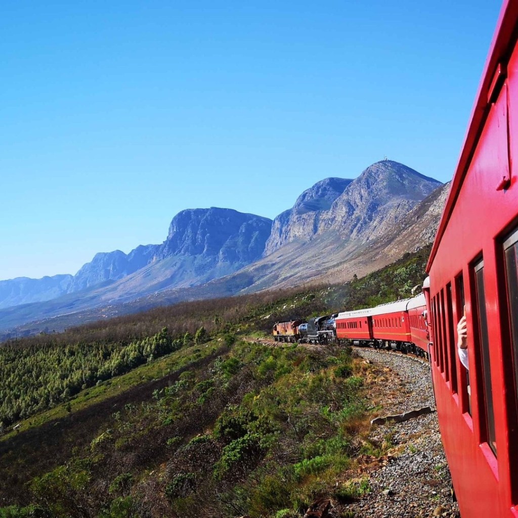 Red train traveling through mountains with scenic valley view.
