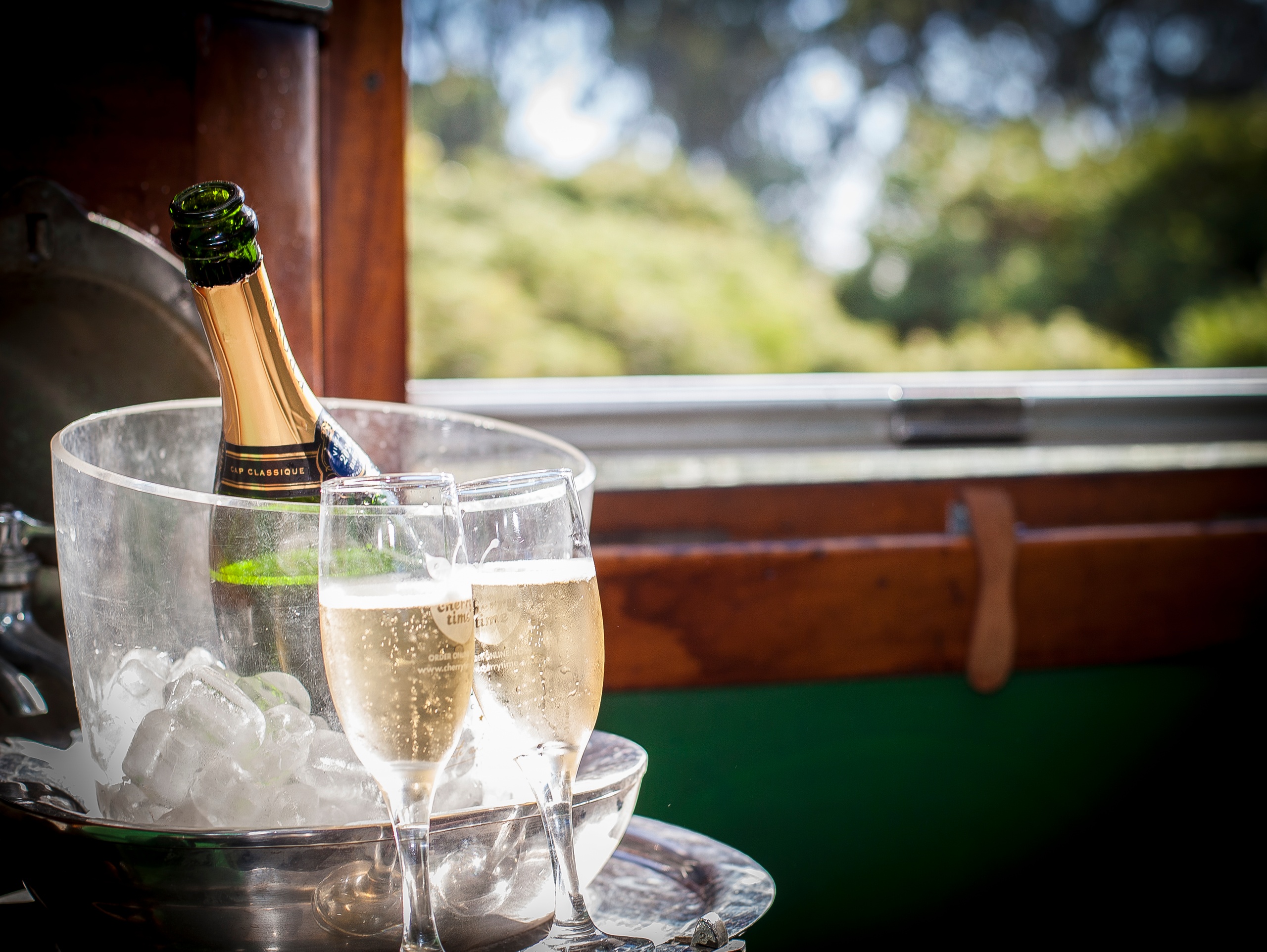 Champagne bottle in ice bucket with two filled glasses by a window.