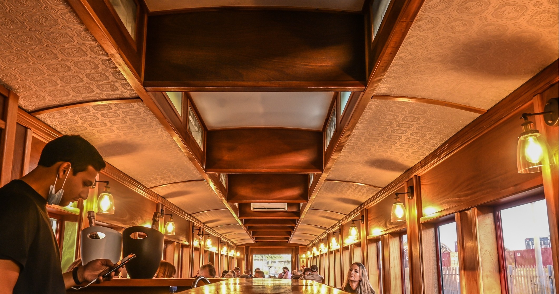 Interior of a vintage train carriage with passengers seated, wood paneling, and warm lighting.