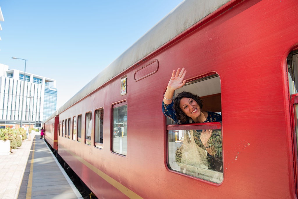 Person waving from a red train window at a station.