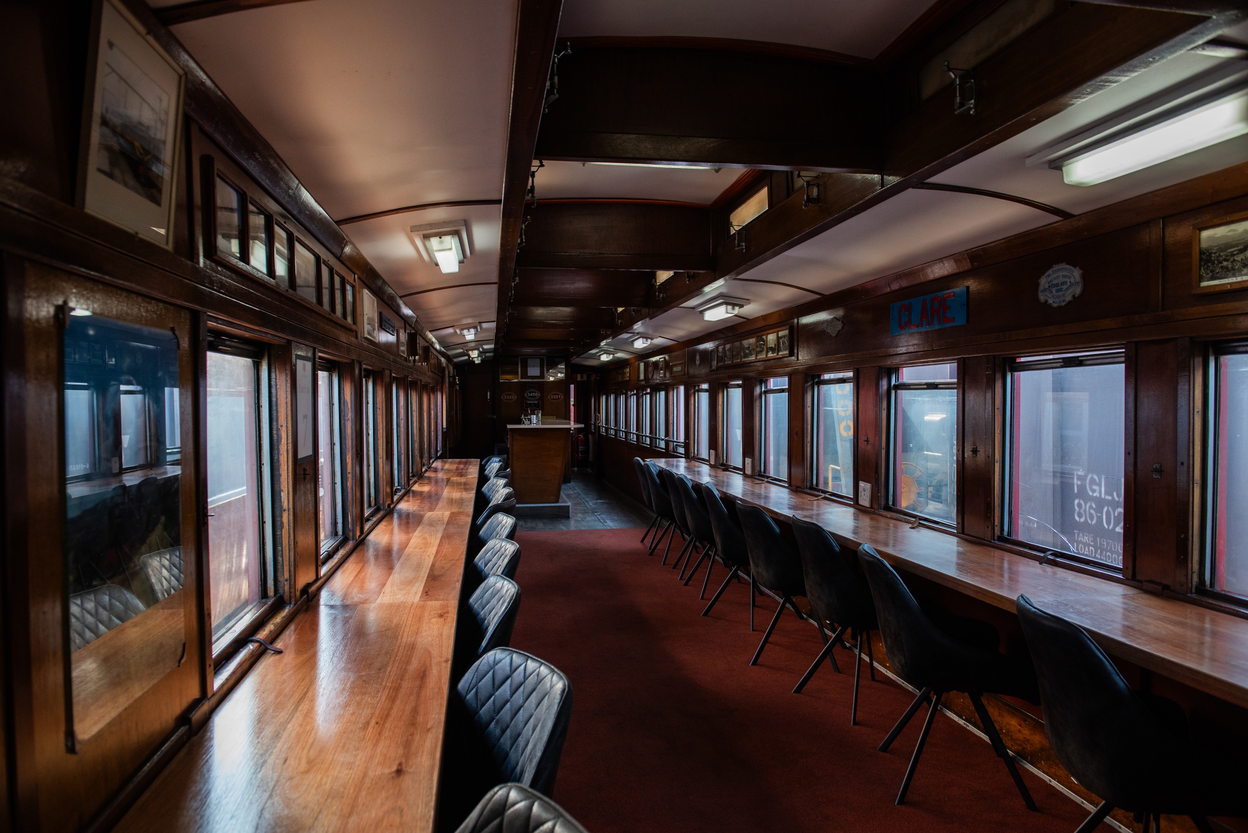 Vintage train car interior with wooden paneling and long rows of chairs.