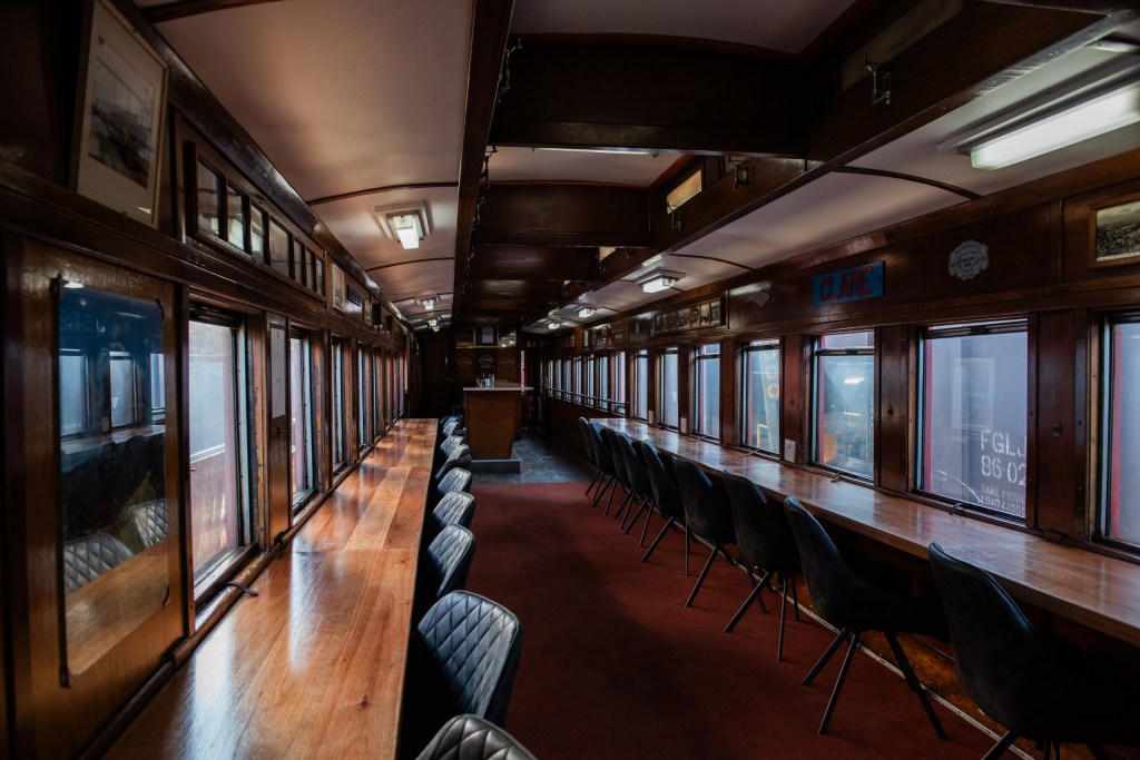 Vintage train car interior with wooden paneling and long rows of chairs.