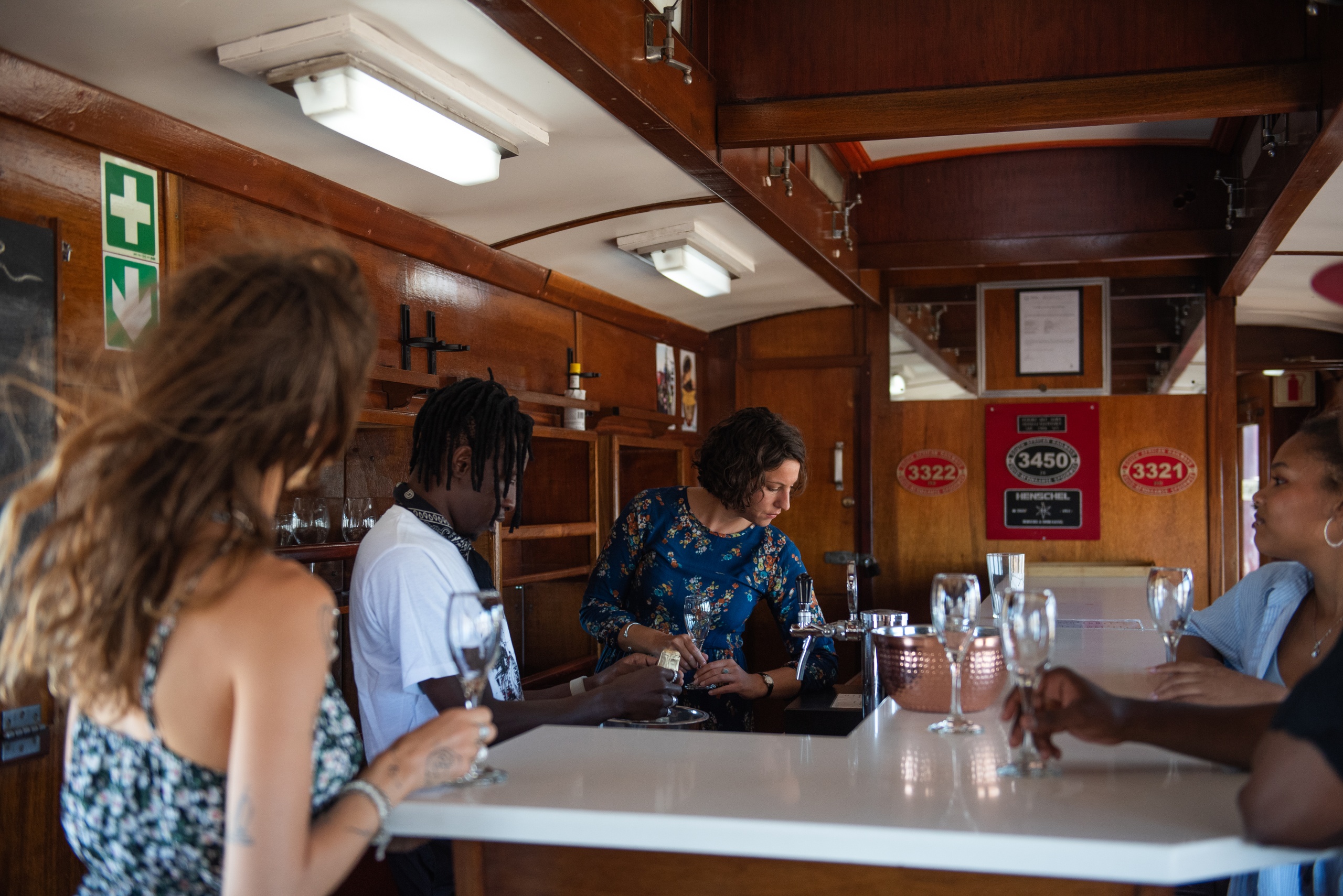 People at a bar inside a vintage train, holding wine glasses.