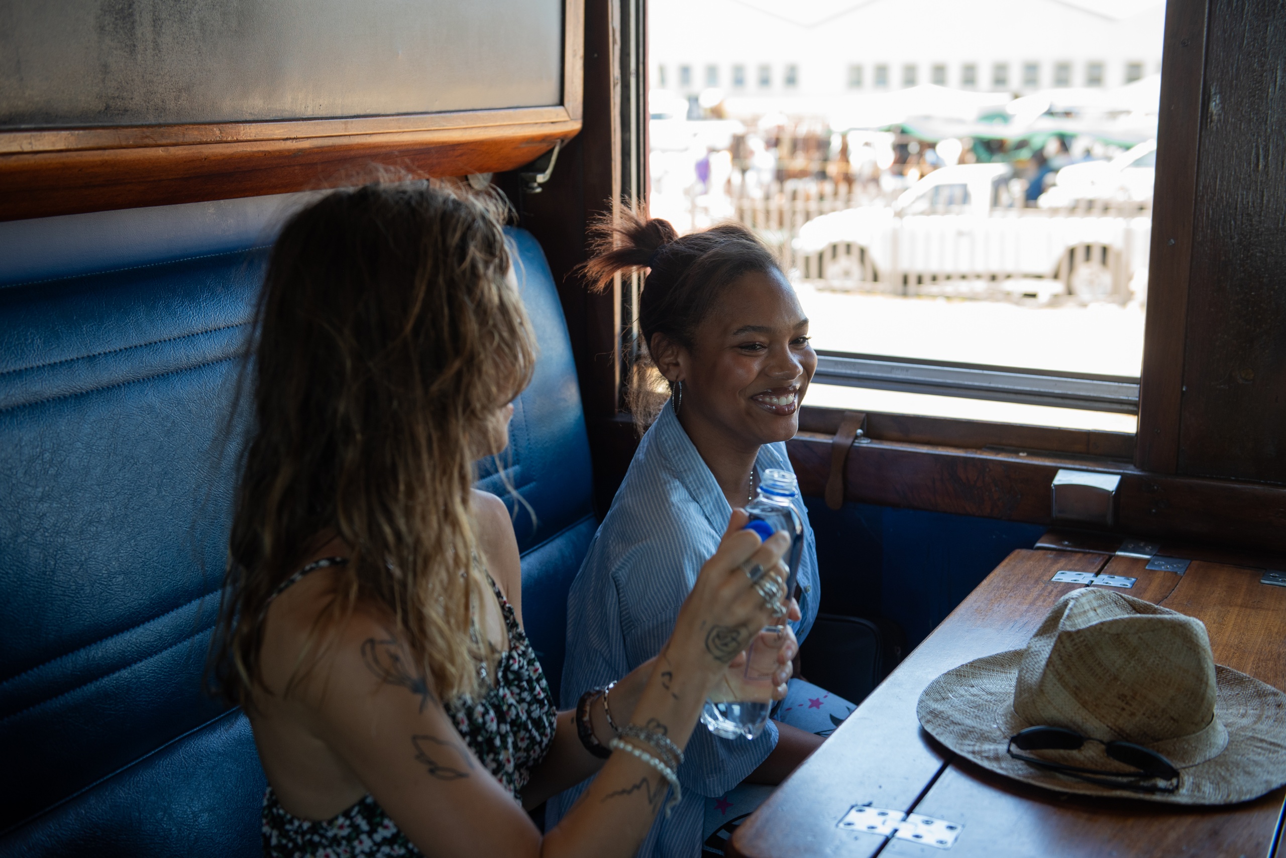 Two people sitting in a train cabin, smiling and holding a water bottle.