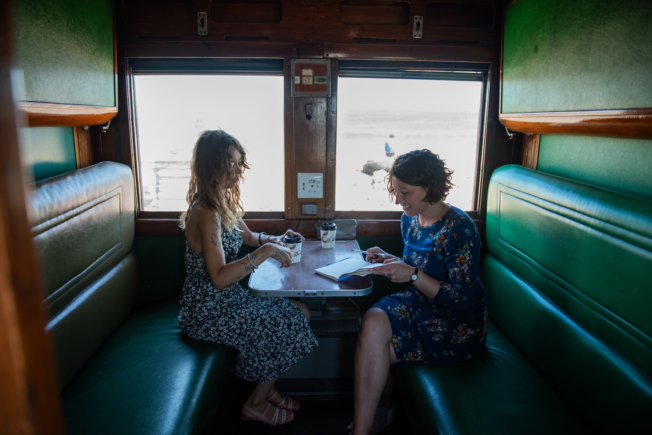 Two women sitting at a table inside a train carriage.