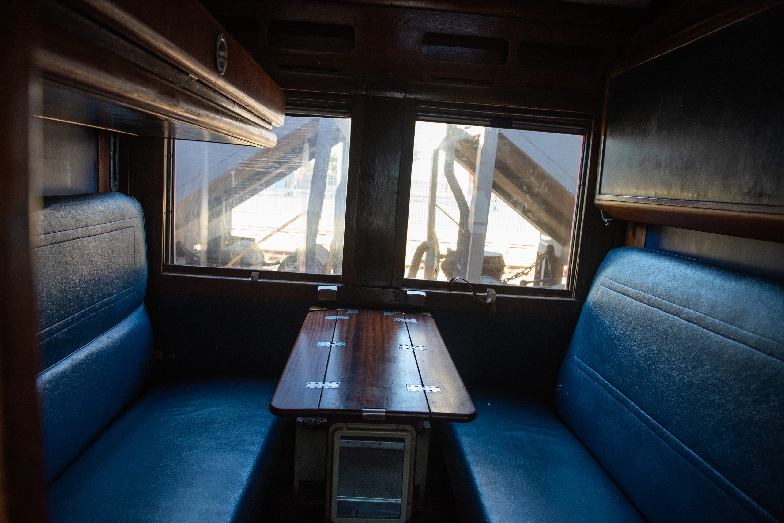 Interior of a vintage train car with blue seats and a wooden table.