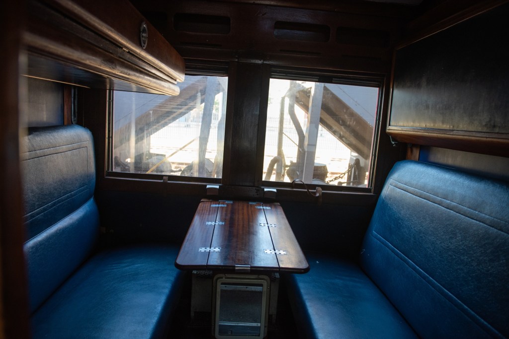 Interior of a vintage train car with blue seats and a wooden table.
