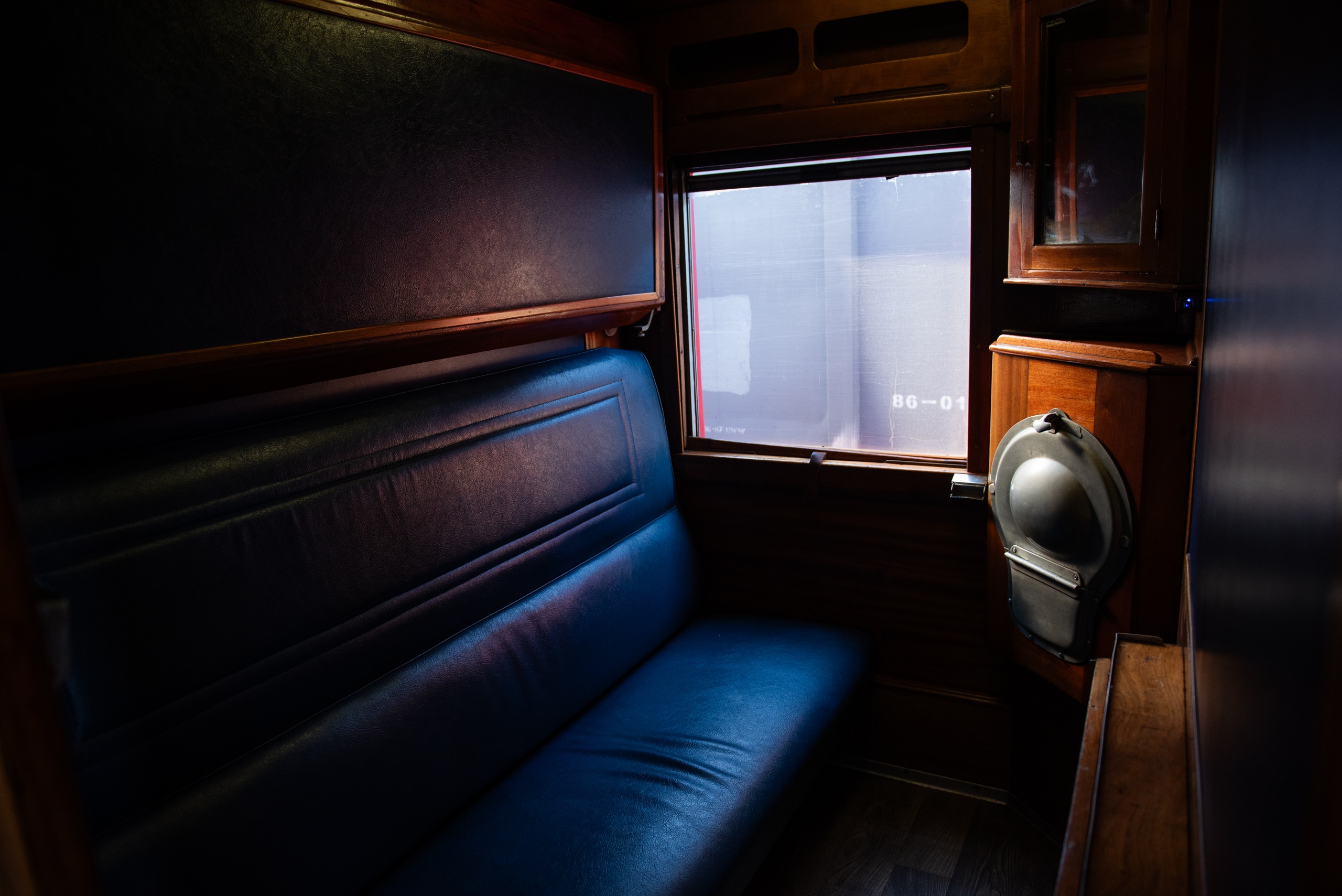 Interior of a dimly lit vintage train cabin with a blue seat and window.