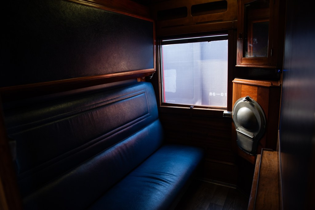Interior of a dimly lit vintage train cabin with a blue seat and window.
