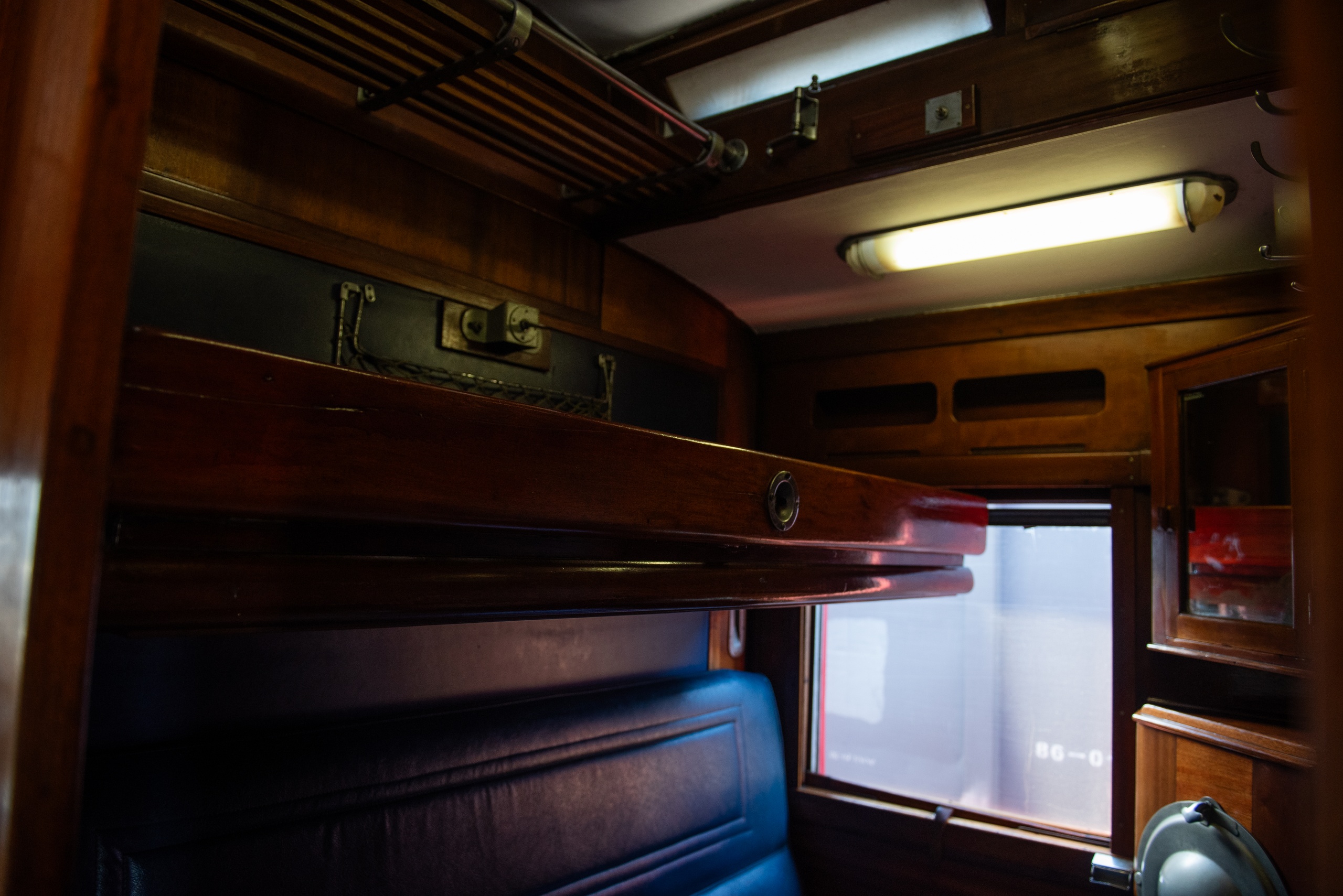 Vintage train cabin with bunk bed and overhead luggage rack.