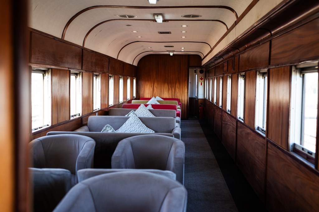 Vintage train car interior with plush chairs and wooden paneling.