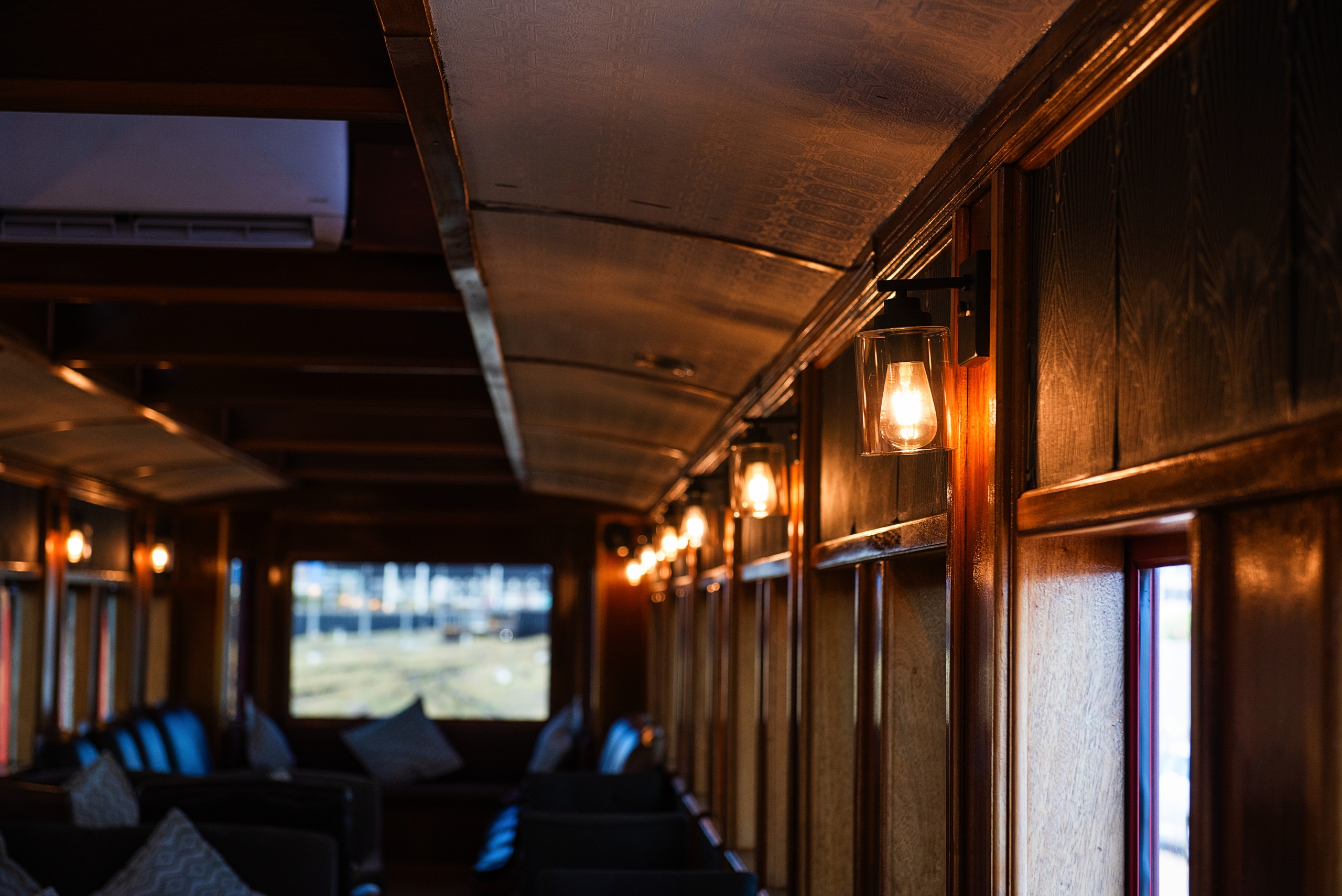 Interior of a vintage train with wooden paneling and lit lamps.