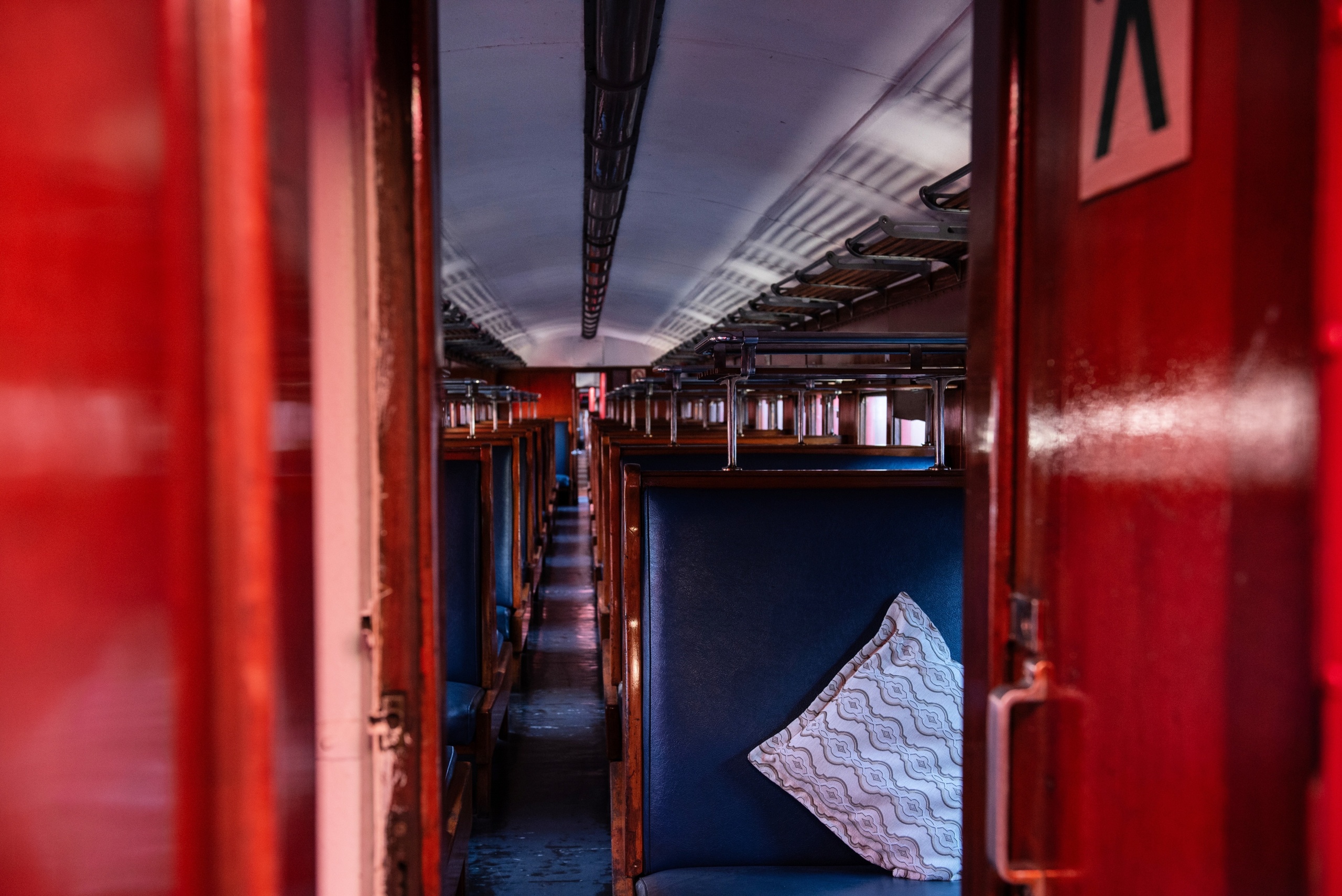 Interior of a vintage train carriage with red walls, wooden seats, and a cushion.