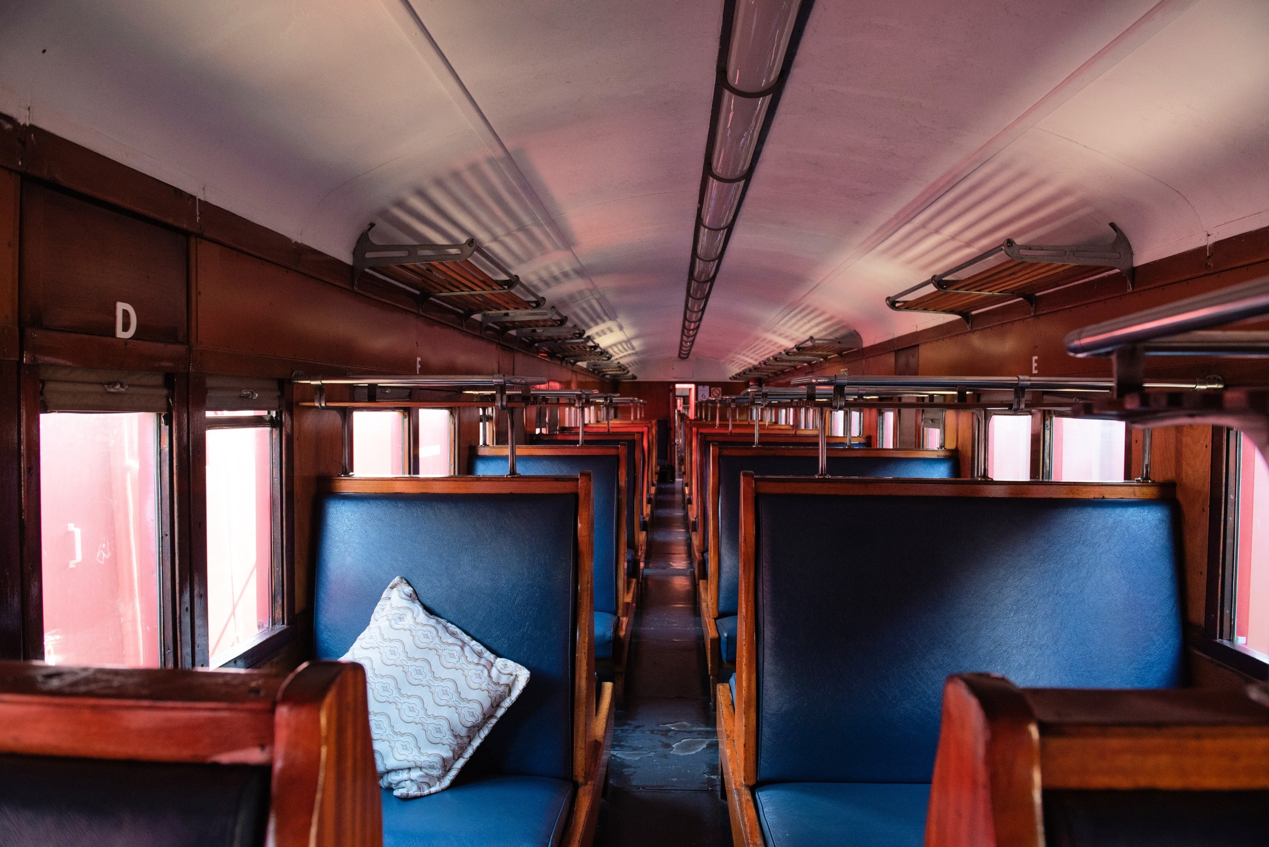 Interior of an empty vintage train with blue seats and a single cushion on one bench.