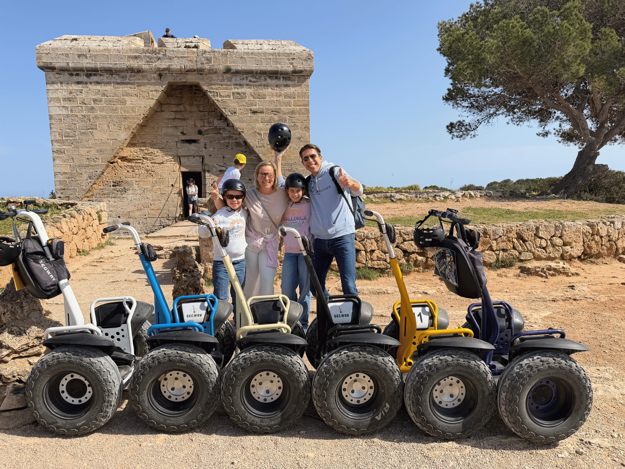 Five people posing with segways in front of a stone building and tree.