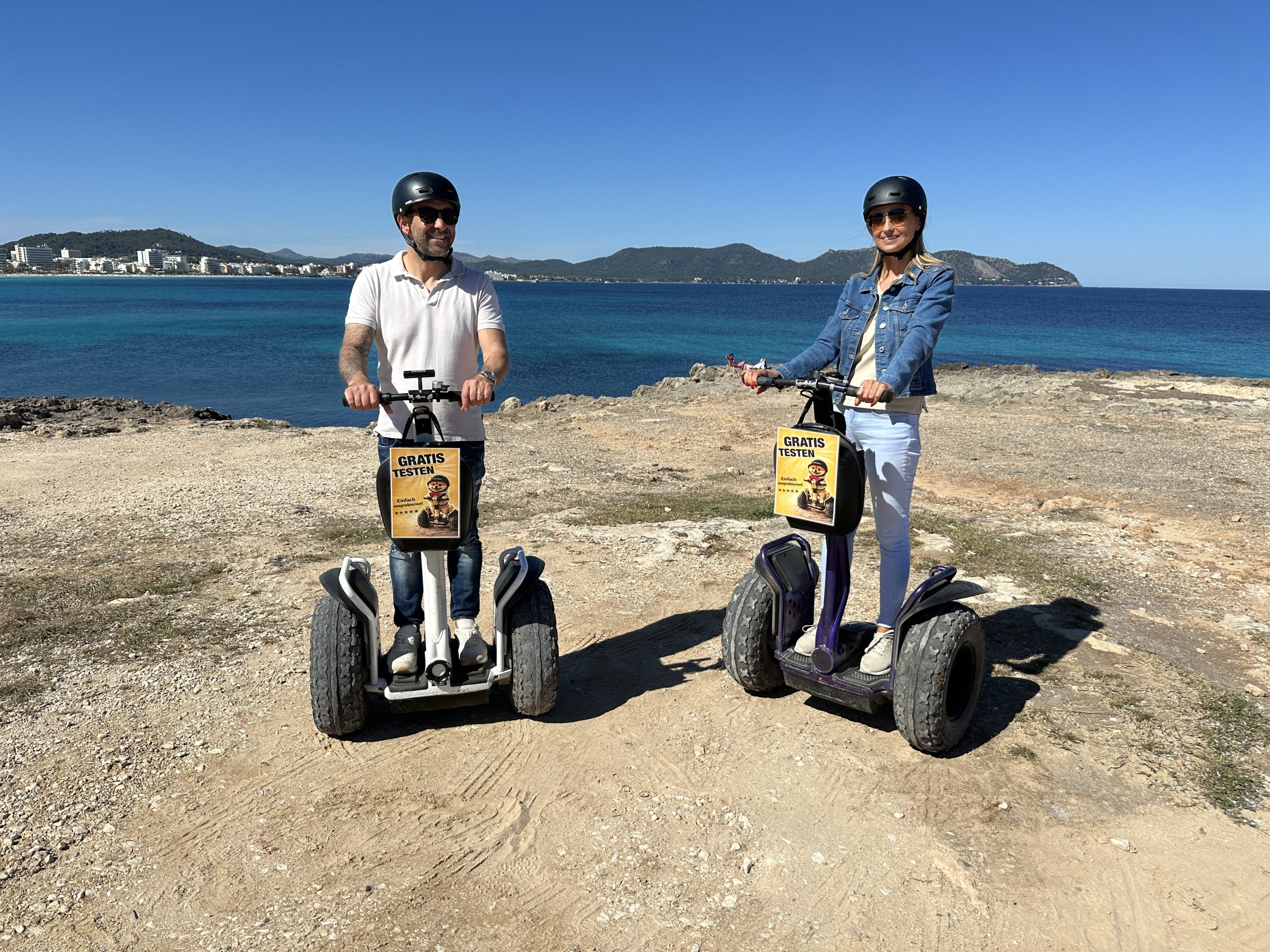 Two people on Segways by the sea under a clear blue sky.