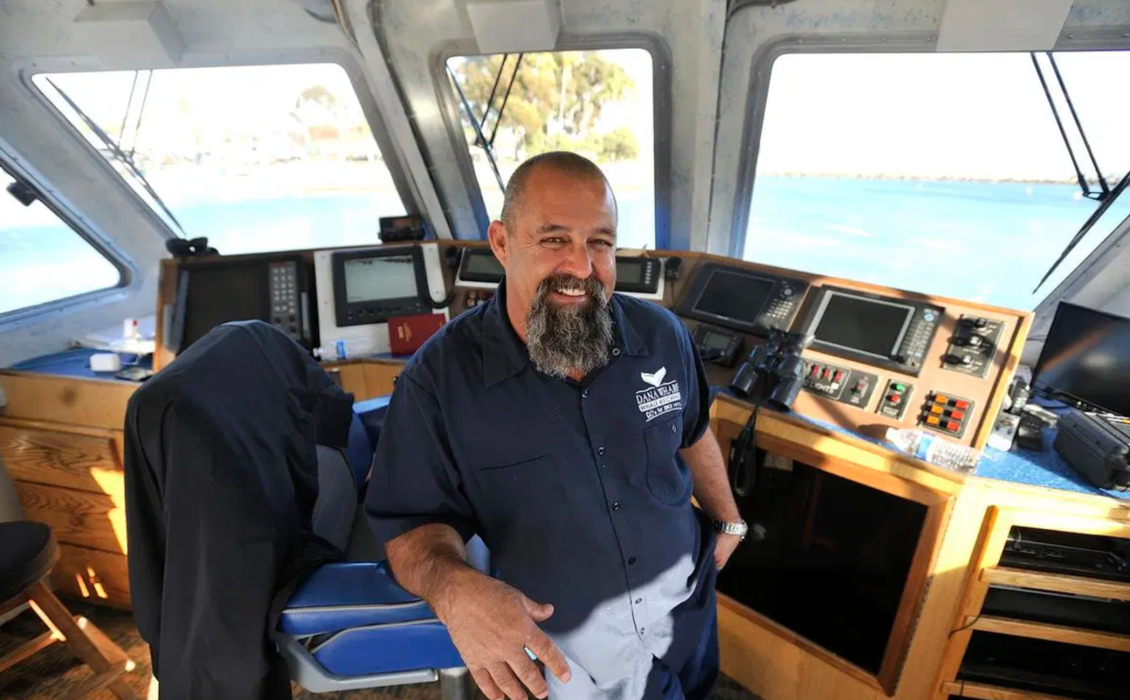 Man smiling on boat's bridge with ocean view in background.