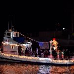 Boat decorated with Christmas lights and a Santa figure at night on water.