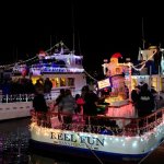 Boats decorated with festive lights and holiday figures at night on the water.