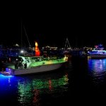 Boats decorated with holiday lights reflecting on water at night.