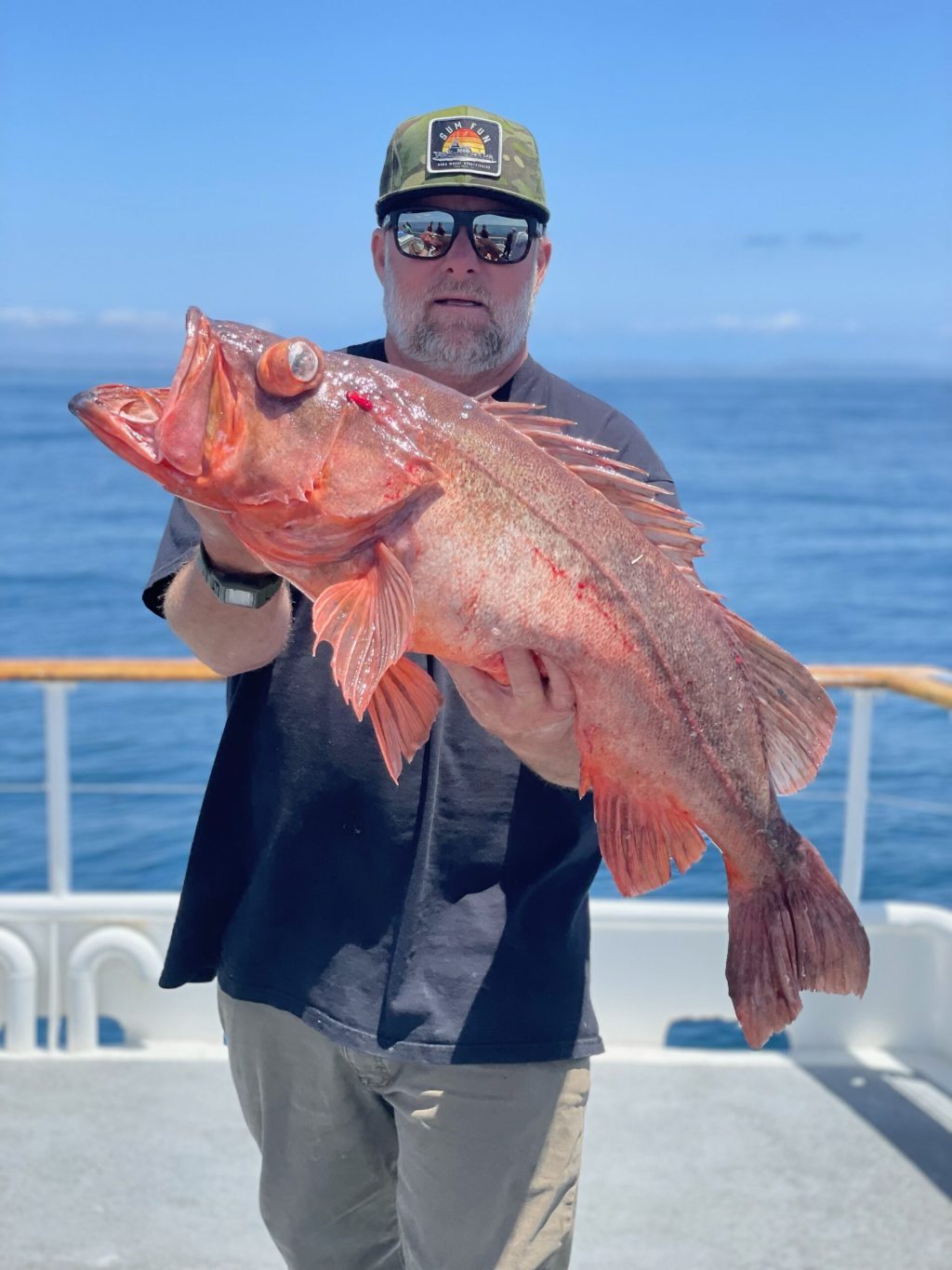 Person holding a large red fish on a boat with ocean in the background.