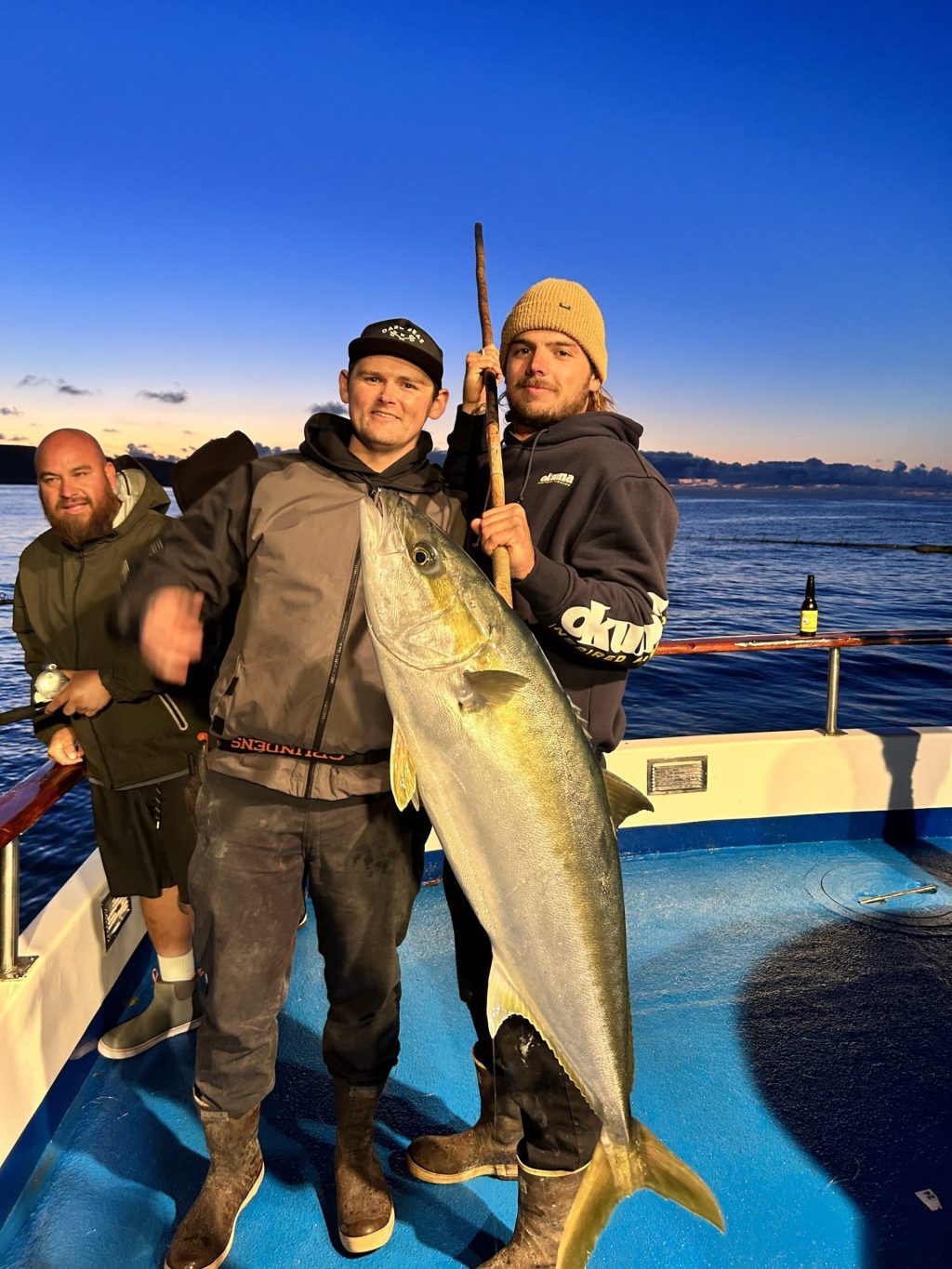Two men on a boat holding a large fish during sunset.