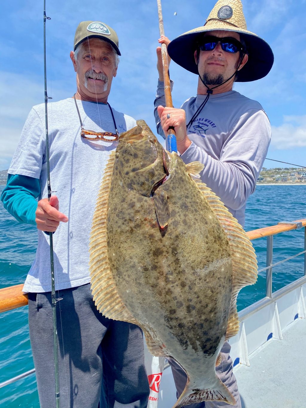 Two men on a boat holding a large fish with the ocean in the background.