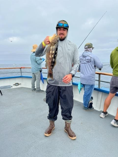 Person holding a fish on a boat with others fishing in the background.