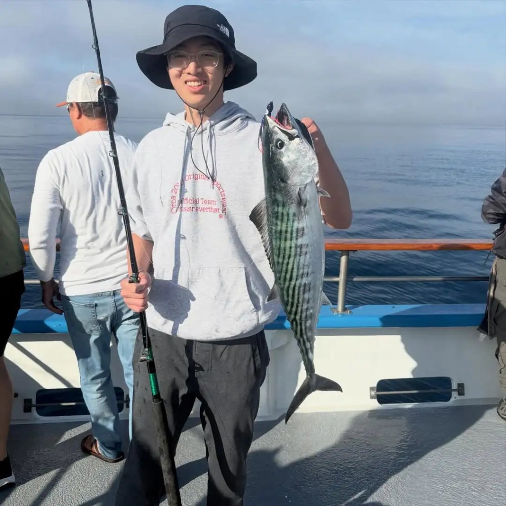 Person on boat holding fishing rod and a large fish, smiling.