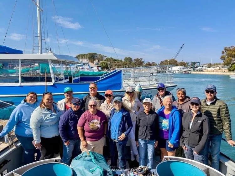 Group of people posing on a boat near a marina under a clear sky.
