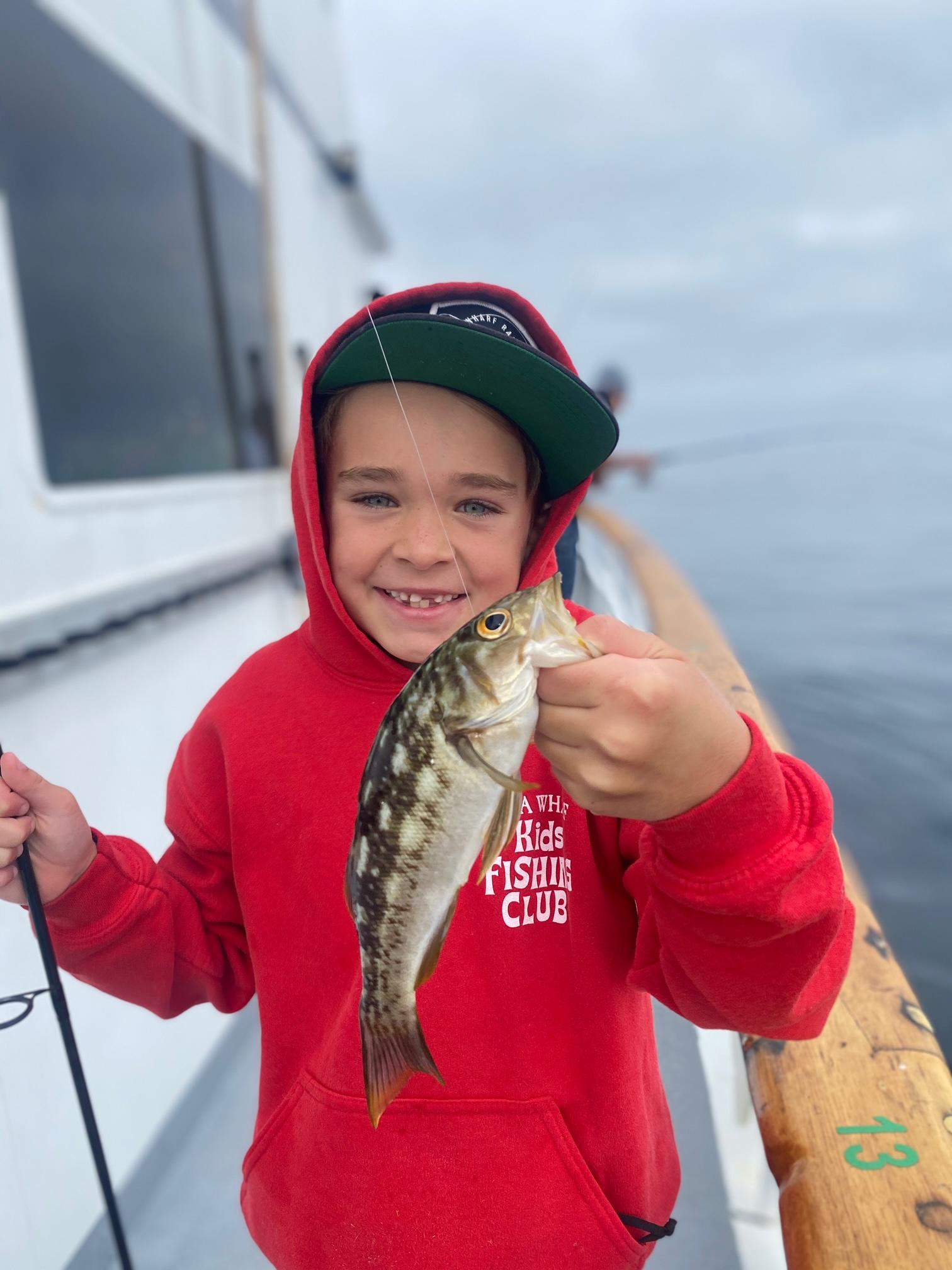 Child in red hoodie holding a fish on a boat.