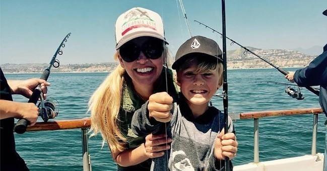 Woman and child holding fishing rods on a boat with ocean in the background.