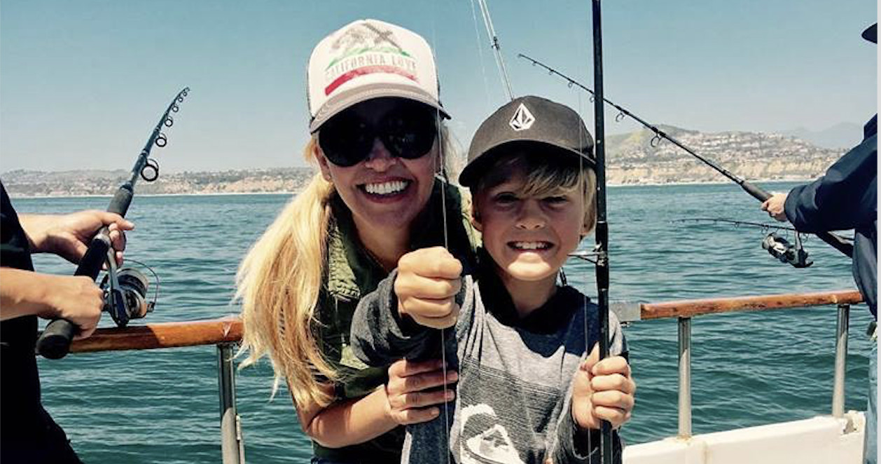 Smiling woman and boy holding a fishing line on a boat with ocean in background.