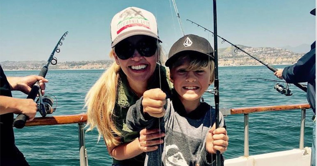 Smiling woman and boy holding a fishing line on a boat with ocean in background.